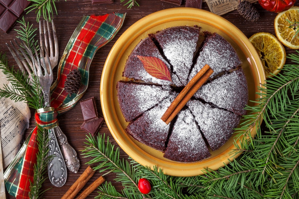 A festive cake surrounded by lemons, cutlery wrapped in a tartan ribbon and Christmas tree foliage